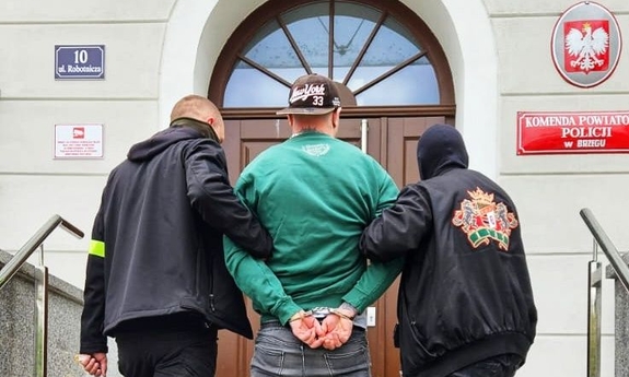 dwaj policjanci prowadzą po schodach do budynku Komendy Powiatowej Policji w Brzegu zatrzymanego mężczyznę zakutego w kajdanki