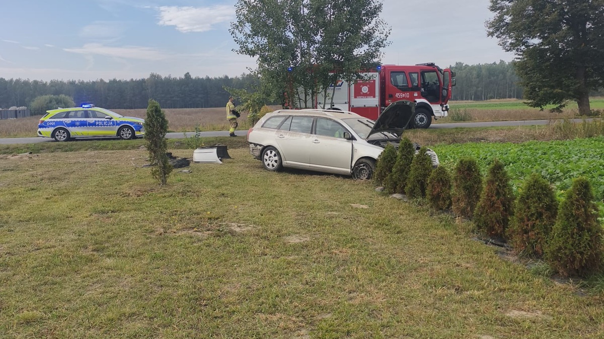 rozbity samochód na prywatnej posesji, w tle widać drogę na której stoi radiowóz i wóz strażacki