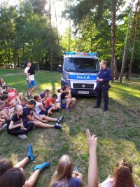 na zdjęciu ukazany jest policjant, który prowadzi z dziećmi spotkanie dotyczące bezpieczeństwa w ruchu drogowym