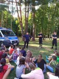 na zdjęciu ukazany jest policjant, który prowadzi z dziećmi spotkanie dotyczące bezpieczeństwa w ruchu drogowym .