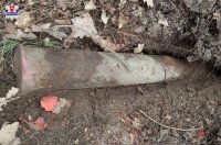 Na pierwszym planie wsrór igliwia znajduje się znaleziony prze saperów pocisk artyleryjski . Leży on na igliwiu i ziemi.