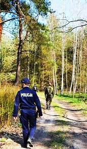 zdjęcie przedstawia policjanta w niebieskim mundurze który patroluje teren leśny za zaginioną osobą