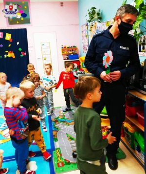 zdjecie przedstawia dzielnicowego który przeprowadza z dziećmi pogadankę na temat bezpieczeństwa