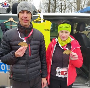 zdjecie przedstawia policjanta z medalem po zakończonym biegu a także pracownika cywilnego z medalem