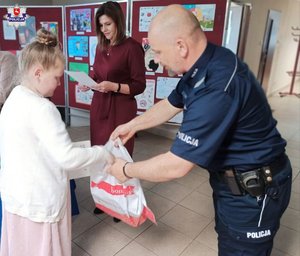 zdjęcie przedstawia policjanta nagradzającego dzieci w konkursie