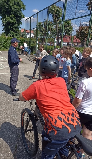 zdjęcie przedstawia policjanta który tłumaczy dzieciom podstawowe zasady w ruchu drogowym