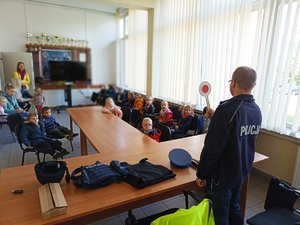 na zdjęciu dzielnicowy na spotkaniu z dziećmi,który trzyma a ręku tarczę i pokazuje przedszkolakom