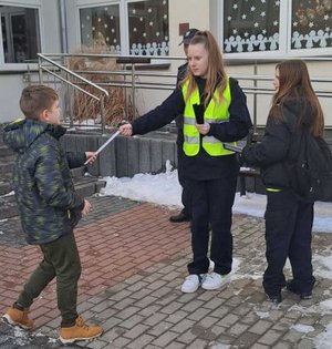 na zdjęciu uczniowie rozdający odblaski z policjantami