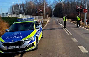na zdjęciu policjant i funkcjonariusz Straży Ochrony Kolei i radiowóz po lewej stronie