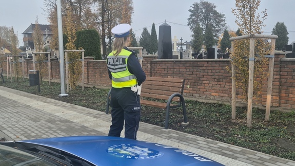 Przed policyjnym radiowozem stoi umundurowana policjantka