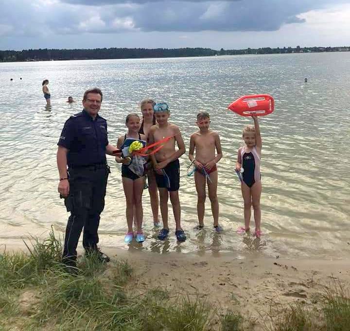 policjant z uczestnikami akcji, w tle widać jezioro
