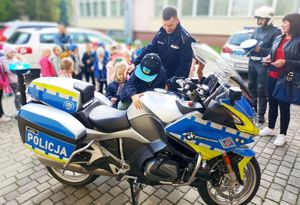 na pierwszym planie motocykl policyjny z policjantem ruchu drogowego ktory pokazuje przedszkolakom sprzet