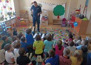 na zdjęciu dzielnicowy,który stoi przed dziećmi i pokazuje im wyposazenie policjanta,dzieci siedząna dywanie